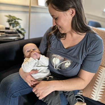 Frau kuschelt mit ihrem Baby während sie mit dem Ardo Hands-Free Pumpset abpumpt