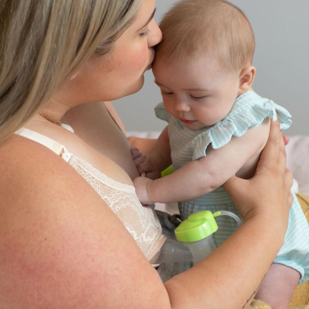 Mutter küsst ihr Baby auf die Stirn während sie abpumpt
