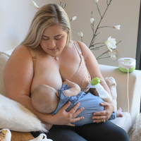 Frau pumpt eine Brust ab während sie an der anderen ihr Baby stillt