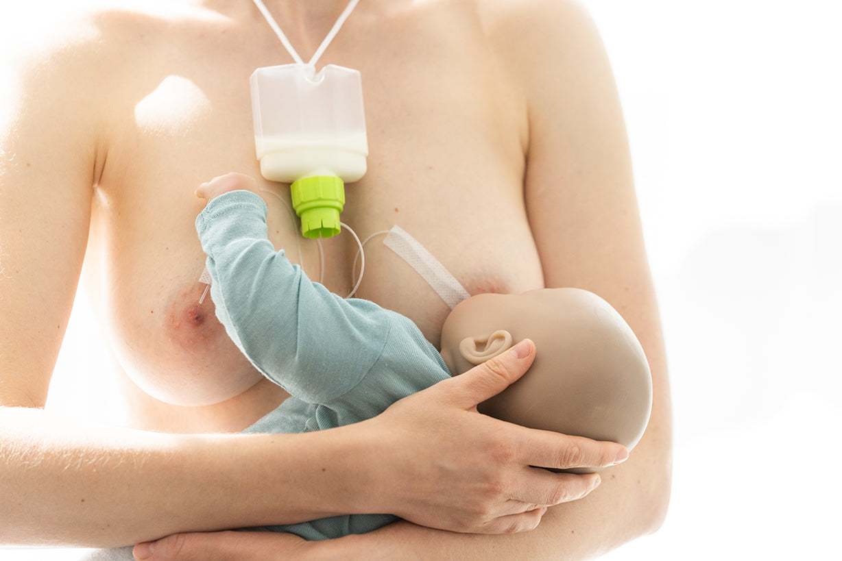 Mutter stillt ihr Baby mit dem Ardo SNS Brusternährungsset; der Milchbehälter hängt vor der Brust und ein dünner Schlauch führt zur Brustwarze.