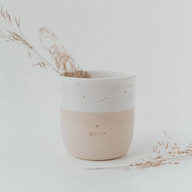 Alleinstehender Eulenschnitt Keramikbecher "Mama" (weiß/beige) auf einem weißen Untergrund, gefüllt mit zarten, getrockneten Gräsern. Minimalistische Boho-Wohnkultur.